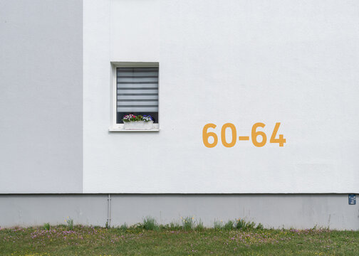 Minimalist architectural landscape framing of a white building facade with a single window featuring a flower box and the numbers 60-64 painted in yellow.