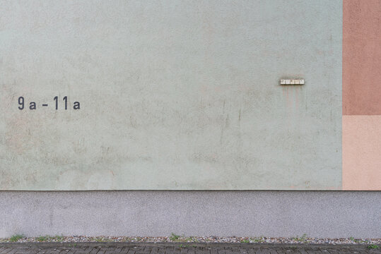 Minimalist graphic architectural view of a pale green plastered residential wall painted with the house numbers 9a-11a next to contrasting vertical brown panels.