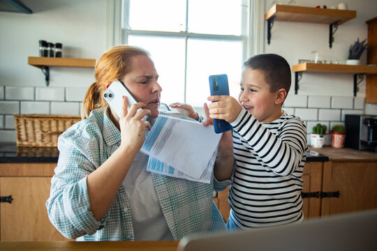 Mother juggling phone call and bills in home kitchen