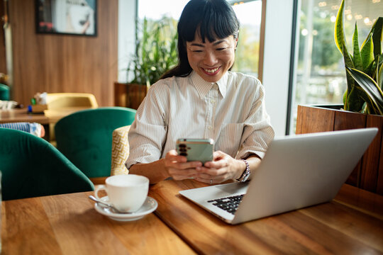 Smiling woman using smartphone and laptop at cafe