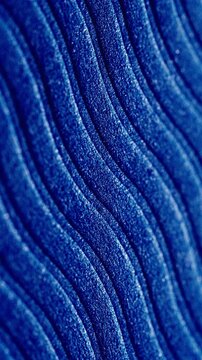 Blue glitter wavy texture slow pan. Close-up of sparkling blue wavy surface with fine glitter particles. Smooth linear camera movement reveals shimmering light reflections across the textured waves.