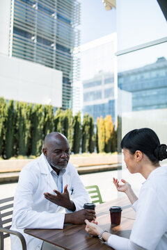 Two doctors discussing patient case during coffee break outdoors