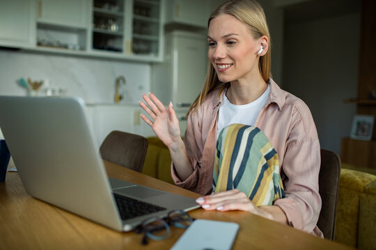 Young woman waving during video call on laptop at home kitchen