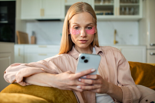 Young woman with under eye patches using smartphone at home