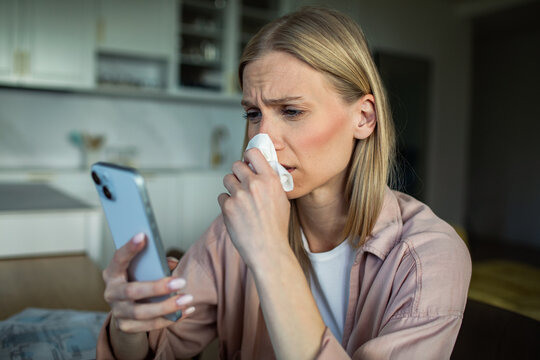 Worried woman with tissue reading smartphone message in home kitchen