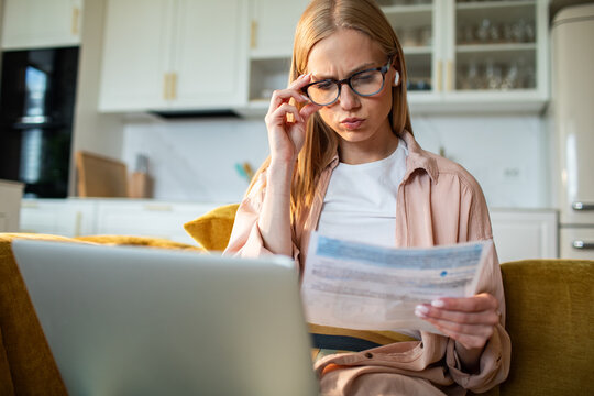 Worried woman reviewing bills with laptop at home