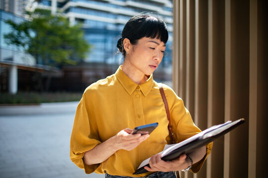 Businesswoman checking phone and documents on city street