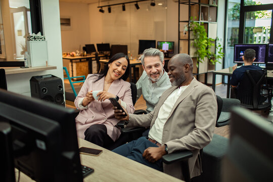 Coworkers viewing a smartphone during a break in a modern open office