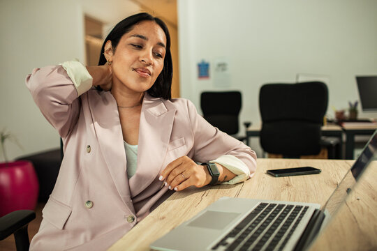 Young businesswoman with neck pain at laptop in modern office