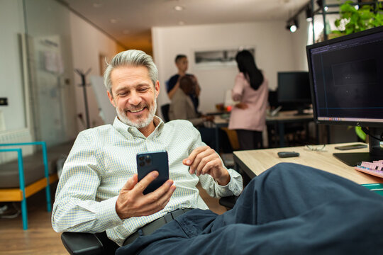 Smiling mature businessman using smartphone at creative office