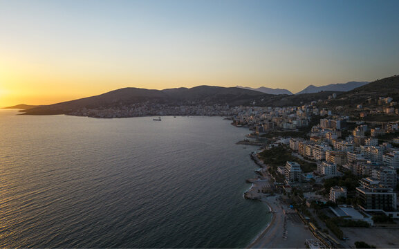Aerial view of Saranda Beach at sunset, featuring the coastal town of Sarande with its buildings, hills, and the Ionian Sea in Sarande, Vlore County, Albania.
