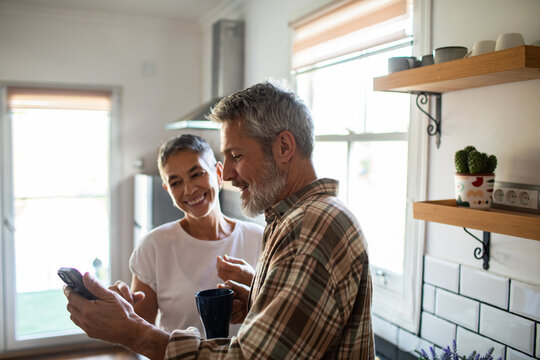 Smiling mature couple using smartphone in bright home kitchen