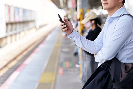 駅のホームでスマートフォンを操作する30代の日本人の男性の会社員の顔無しの匿名イメージ