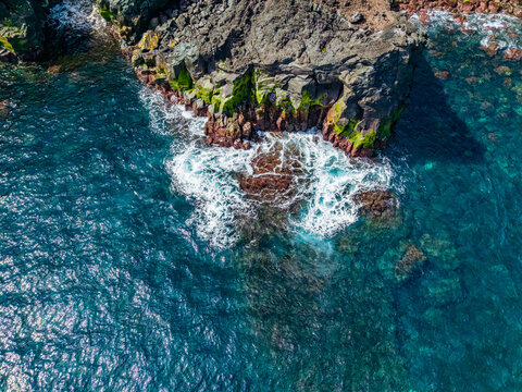 Aerial view of the rugged volcanic coastline at Miradouro das Pedras Negras with crashing waves and deep blue Atlantic waters in Sao Miguel, Acores, Portugal.