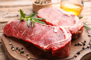 Fototapeta premium Raw beef steak with spices, rosemary and oil on wooden table, closeup