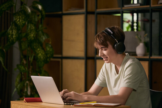 Smiling teen boy learning online with laptop and headphones at home. Concept of edtech, remote school, digital education, home study and youth lifestyle.