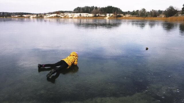 Little girl in the yellow jacket crawling on a slippery frozen lake.