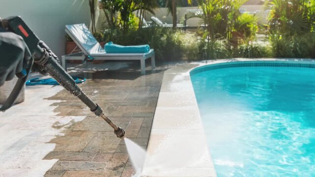 Person power washing poolside tiles for outdoor cleaning and maintenance on a sunny day