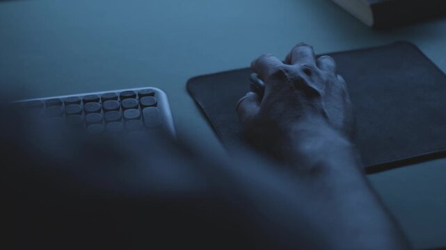 Developer working on a code at night, close-up of hand on mouse