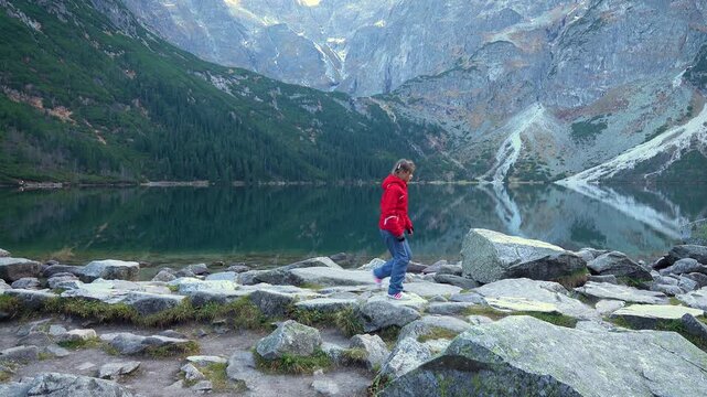 teenager girl with tourist backpack walks along stony shore of lake Eye of Sea (Morskie Oko) in Tatra Mountains, Poland