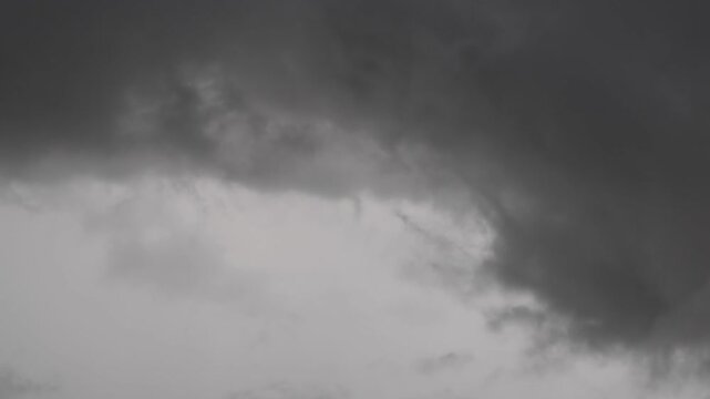 Ominous, swirling black clouds against a gray sky&mdash;a dramatic darkness associated with rain or a storm.