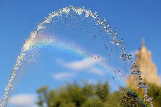 A fountain's water jet arching against a blue sky with sunlight creating glints.