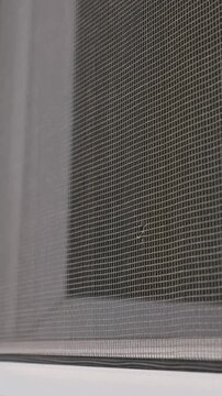 A grey protective mosquito net attached to a white window frame features a small torn hole in the mesh material. Concept of home maintenance, pest control, and household repair necessities.
