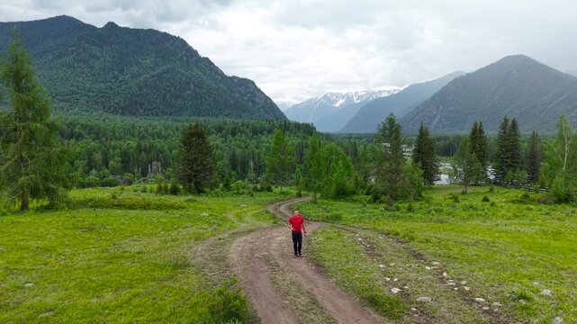 Cinematic drone tracking shot of an athletic male hiker walking forward along a remote path towards distant snowy mountain ranges near Tyungur.