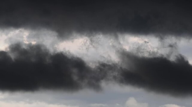 Ominous, swirling black clouds against a gray sky&mdash;a dramatic darkness associated with rain or a storm.