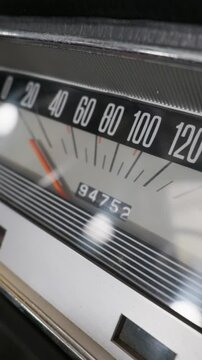 A close-up view of a vintage car speedometer shows the needle at zero mph with retro typography. The dashboard features polished chrome trim and a mechanical odometer displaying mileage.