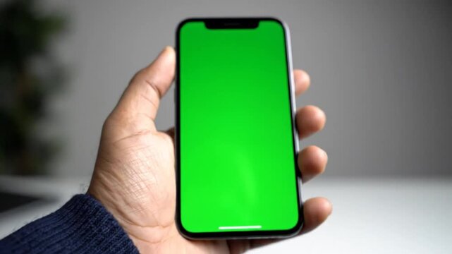 Hand holding iPhone with green screen display, perfect for adding your own content, advertisement, or information.