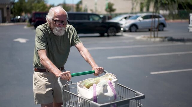Senior man smiles as he pushes a cart with groceries through the empty parking lot on a sunny day.