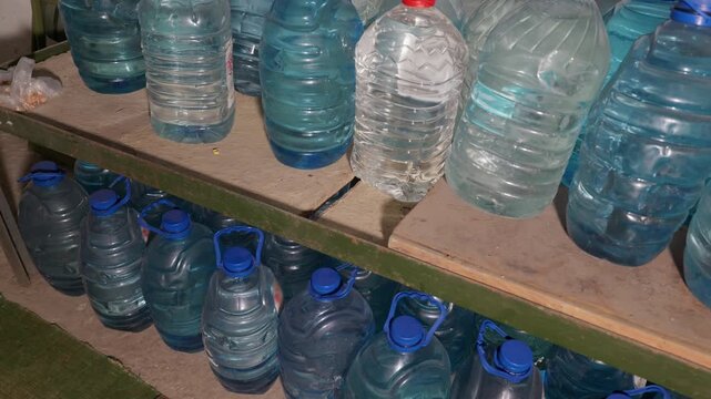 Large plastic bottles filled with drinking water stand arranged on rustic wooden shelves inside a storage room. Concept of emergency preparation, survival resources, and clean hydration.