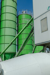 Green industrial silos and storage tanks at a concrete batching plant under a clear blue sky, modern eco-friendly construction industry and manufacturing infrastructure © kalyanby