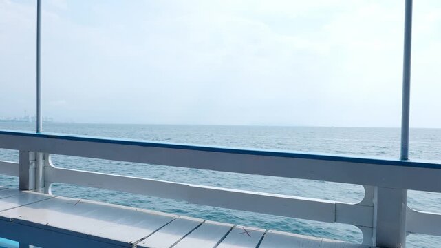 Empty seating and white railing on a passenger ferry deck overlooking calm blue sea, a hazy horizon and distant coastal skyline, conveying peaceful maritime travel and relaxation.