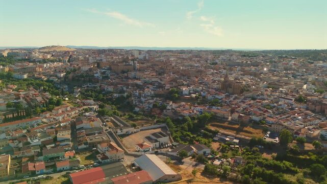 Drone flies backward from the historic center of Caceres, gradually revealing the full extent of the city surrounded by green Extremadura landscape.