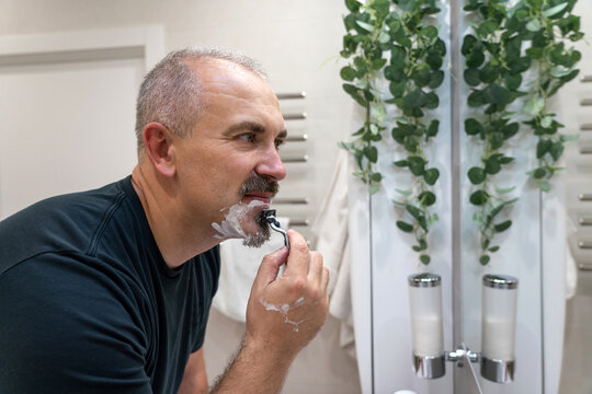Man shaving with razor using foam in bathroom in the morning