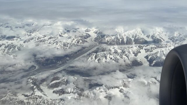 Snowy mountain range with glaciers running between them. Aerial shot from an airplane.