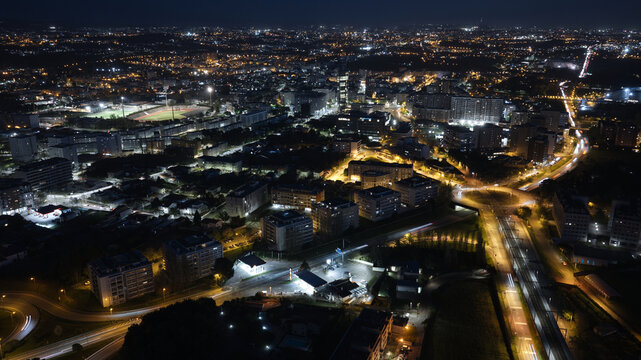 Aerial view of the city of Maia at night, featuring illuminated streets, residential buildings, a sports stadium, and light trails from traffic in Maia, Porto District, Portugal.