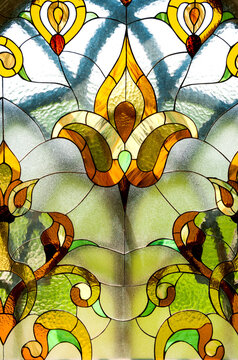 Ornate stained glass window features symmetrical floral motifs in yellow tones