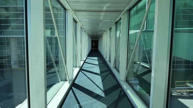 Contemporary airport architecture featuring transparent glass tunnel walkway. Futuristic passenger boarding bridge leading to airplane gate with reflection and perspective view inside terminal.
