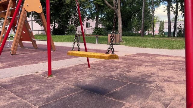 Yellow swing seat hanging on chains in an empty children's playground