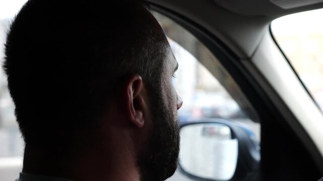 Confident bearded man looking concentrated to urban road while riding electric automobile. Guy driving the auto at highway. Serious male driver operating a motor car at town. Slow motion