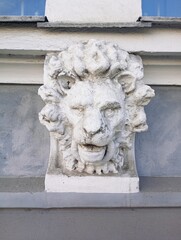 Architectural detail of an antique white stone lion head sculpture on a classic building facade. This historical stone mascaron carving features a fierce leonine expression with a thick wavy mane and  © Oksana