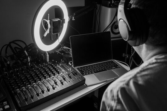 Music producer working in a home recording studio with audio mixing console, laptop, and ring light, classic monochrome edit.