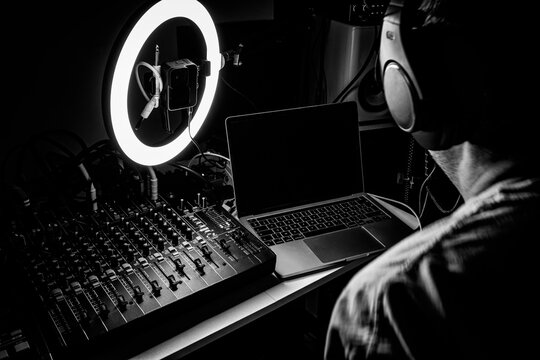 Music producer working in a home recording studio with audio mixing console, laptop, and ring light, presented in a high-contrast black and white style.