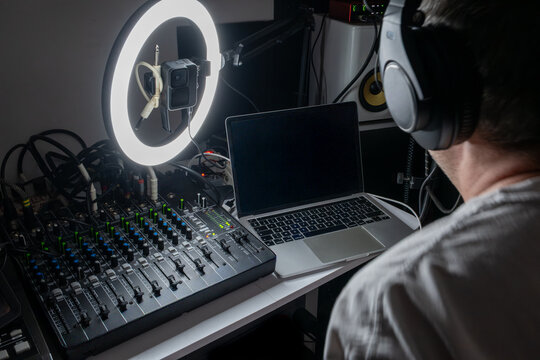 Music producer working in a home recording studio with audio mixing console, laptop, and ring light, natural interior lighting setup.
