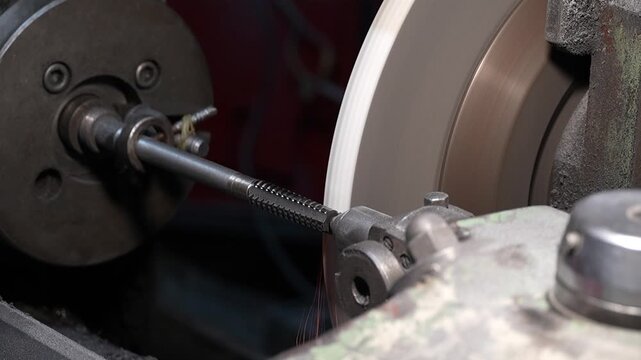 Close up of precision metal threading process on industrial grinding machine in workshop. Rotating steel rod and abrasive wheel during manufacturing operation show machining technology and engineering
