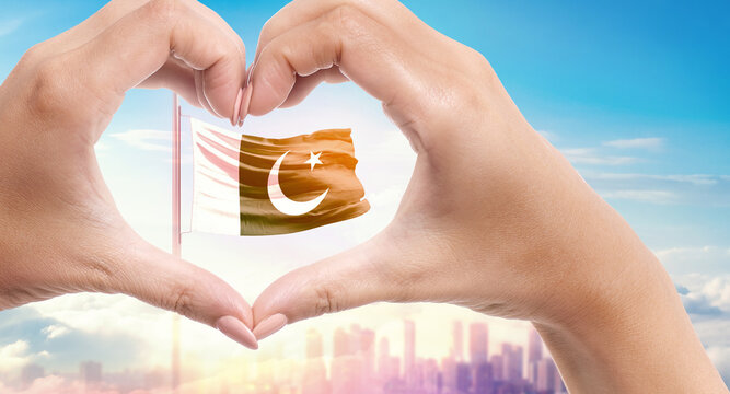 Pakistan national flag. Two hands forming a heart shape in front of a national flag waving in beautiful clouds. Pakistan national flag behind the heart shape hand.