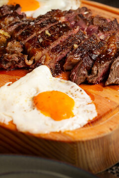 Sliced medium-rare beef steak with two fried eggs served on a wooden board.